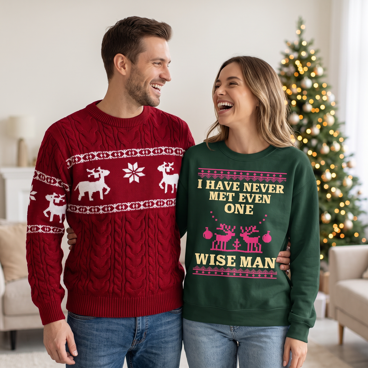 A couple laughing by a Christmas tree, him in a red reindeer knit sweater and her in a green 'I have never met even one wise man' sweatshirt